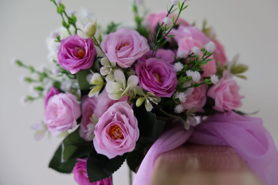A bouquet of fresh pink and white roses with delicate white miniature daisies, green foliage, and small buds arranged together. The flowers are wrapped in soft pink tissue paper tied with a matching r