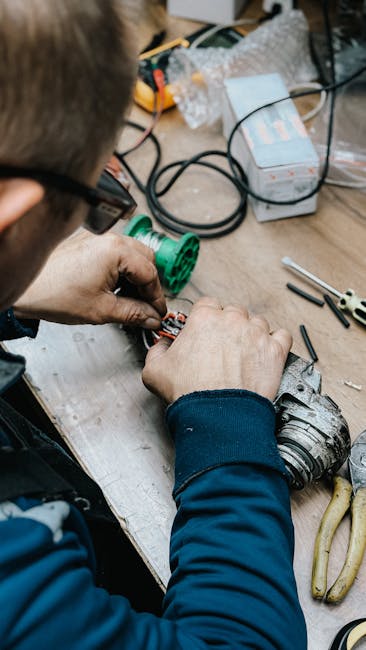 A close-up of a person working on floral wiring, with hands carefully adjusting wiring on stems of fresh flowers. The workstation includes various tools such as pliers, wire cutters, and electrical wi